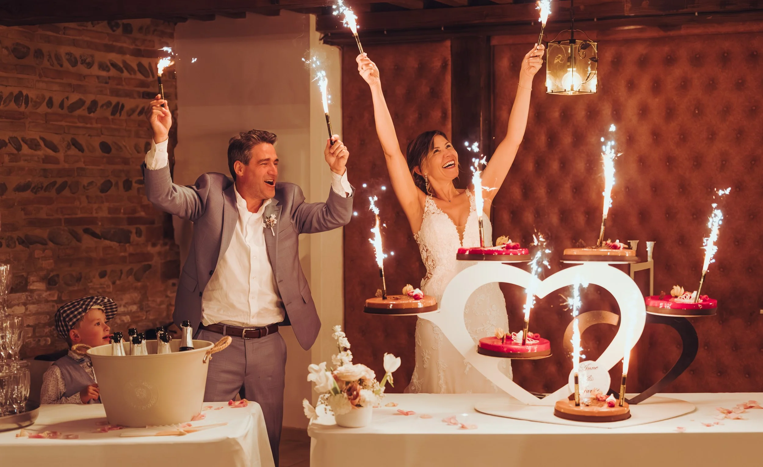 Un couple fête leur mariage avec des gâteaux et des feux d'artifice, entouré d'amis et famille dans une salle chaleureuse au domaine de Lalanne proche de Toulouse