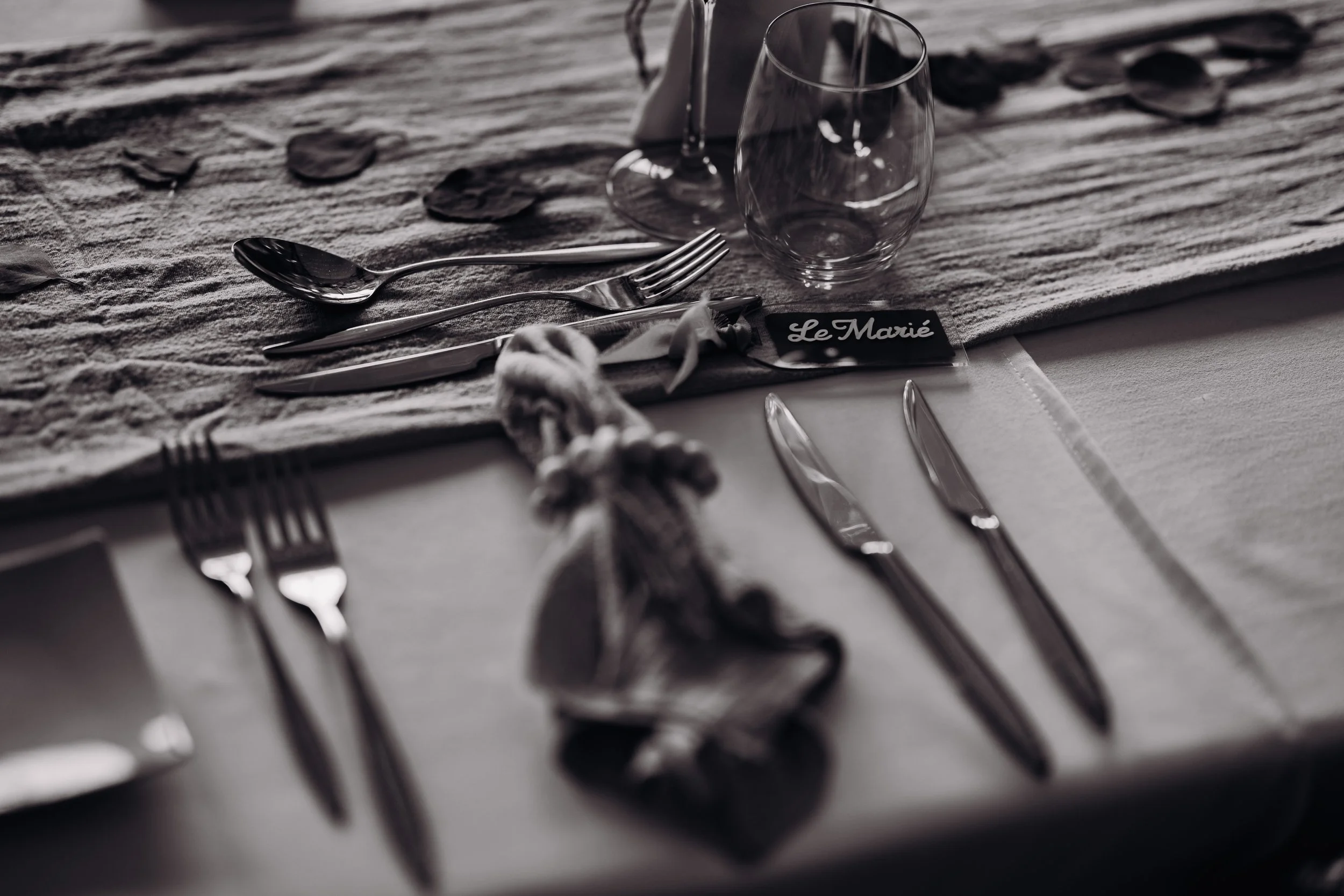 Une table de banquet de mariage proche de Toulouse, en Occitanie, élégante avec des couverts en argent, des verres en verre, une nappe blanche, une nappe en tissu rugueuse, et une étiquette 'Le Marié' pour une cérémonie de mariage.