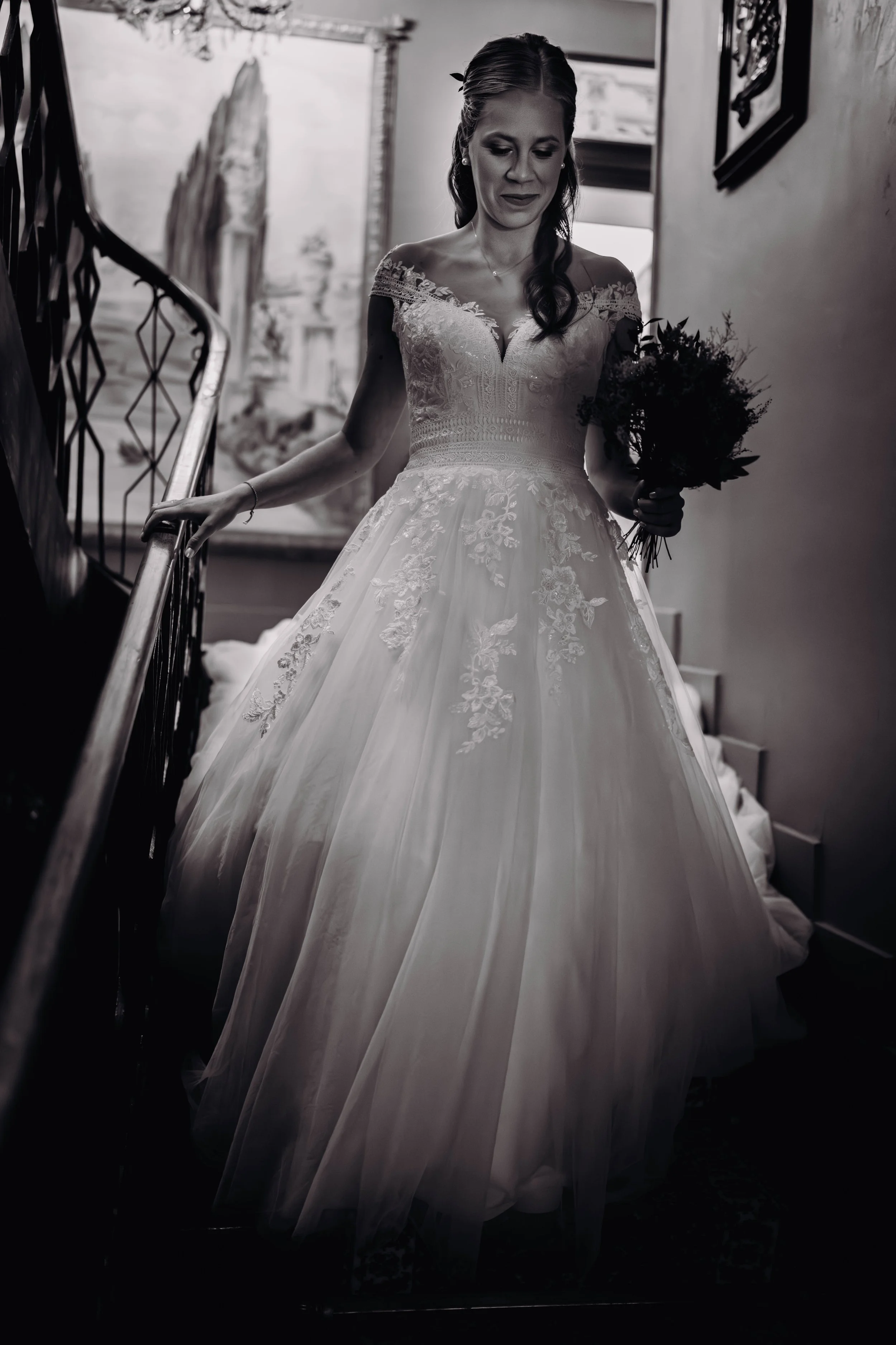 Une femme en robe de mariée blanche tenant un bouquet, marchant dans une maison, en noir et blanc.