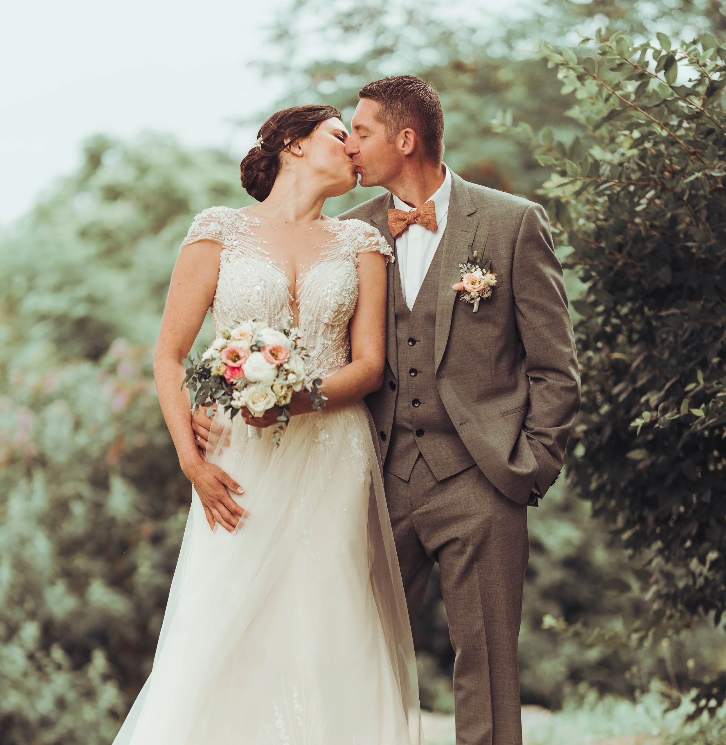 Un couple de mariés échange un baiser lors de leur mariage en extérieur, entouré de nature verdoyante à Fontenilles proche de Toulouse.