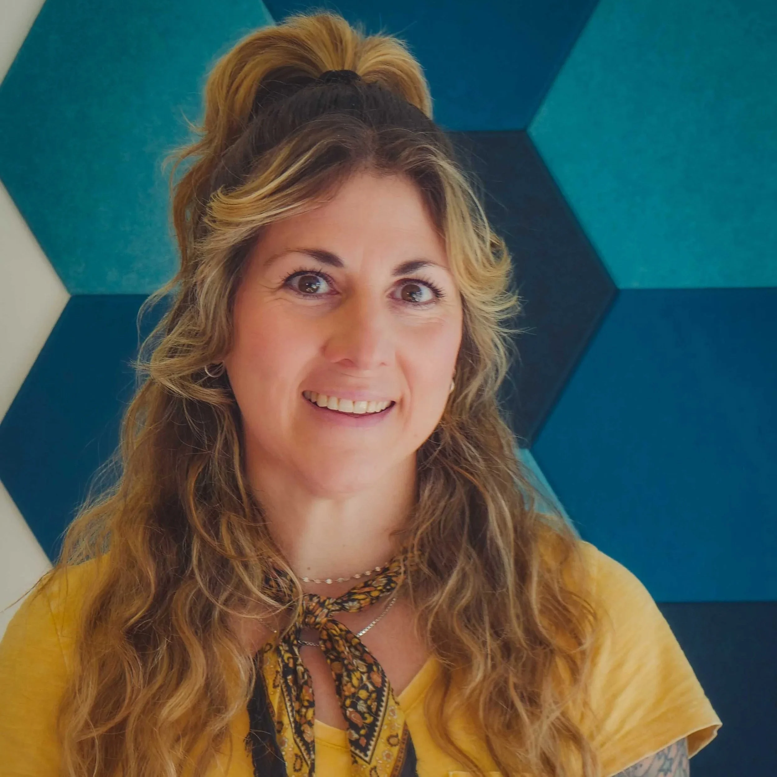 Smiling woman with wavy hair in front of blue geometric wall pattern.