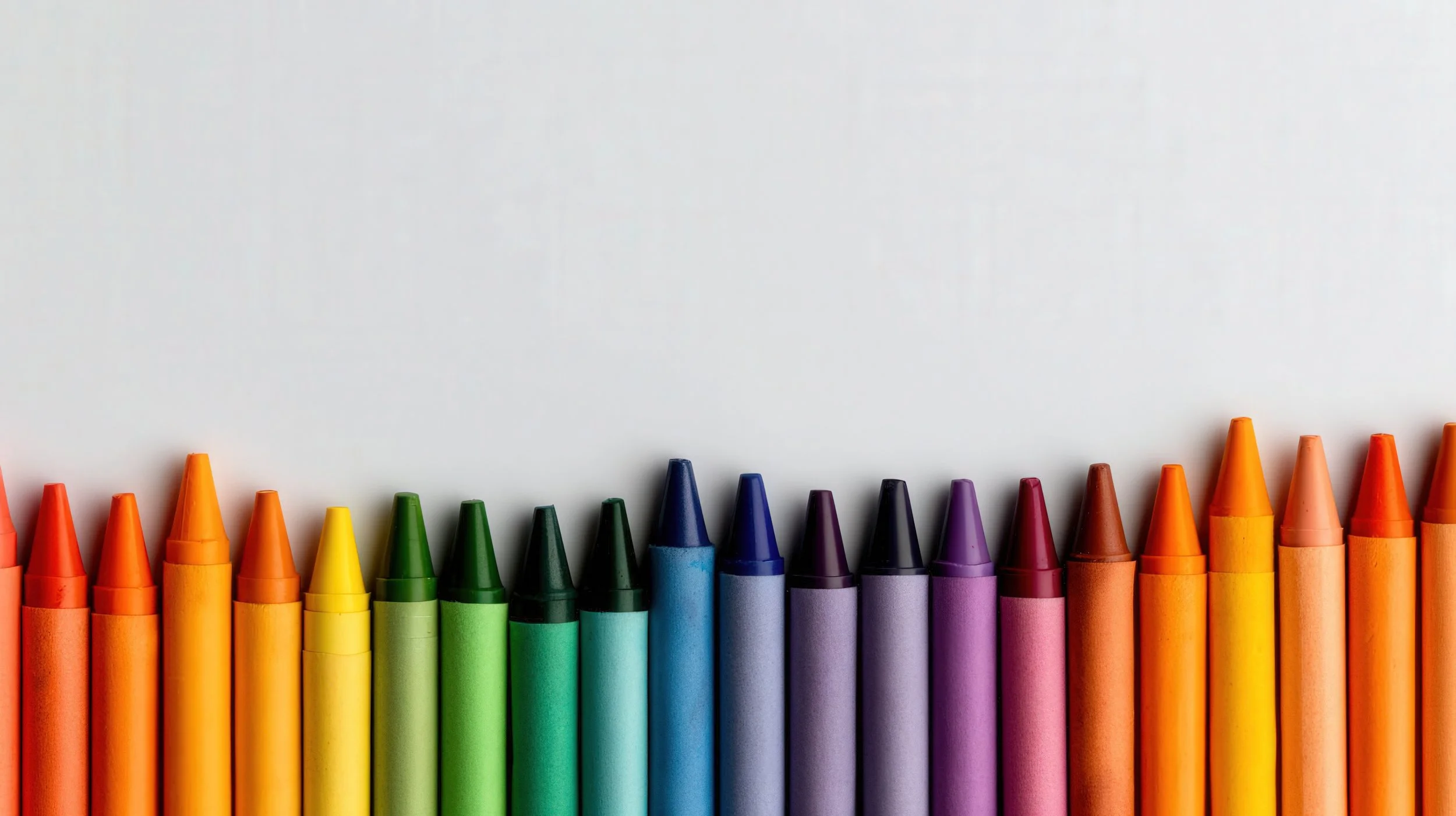 A row of colorful crayons arranged from red to brown on a white background.
