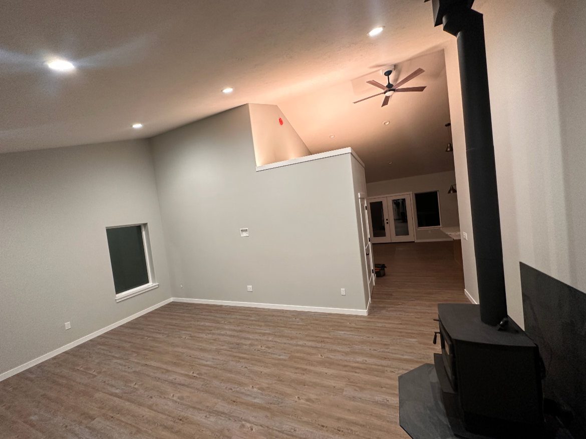 Empty living room with wood flooring, a window, a black wood stove, a ceiling fan, and recessed lighting.