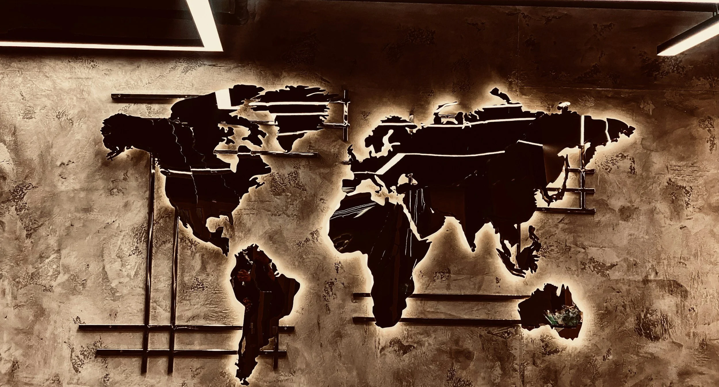Black metal world map wall decor with backlighting, mounted on a textured beige wall.