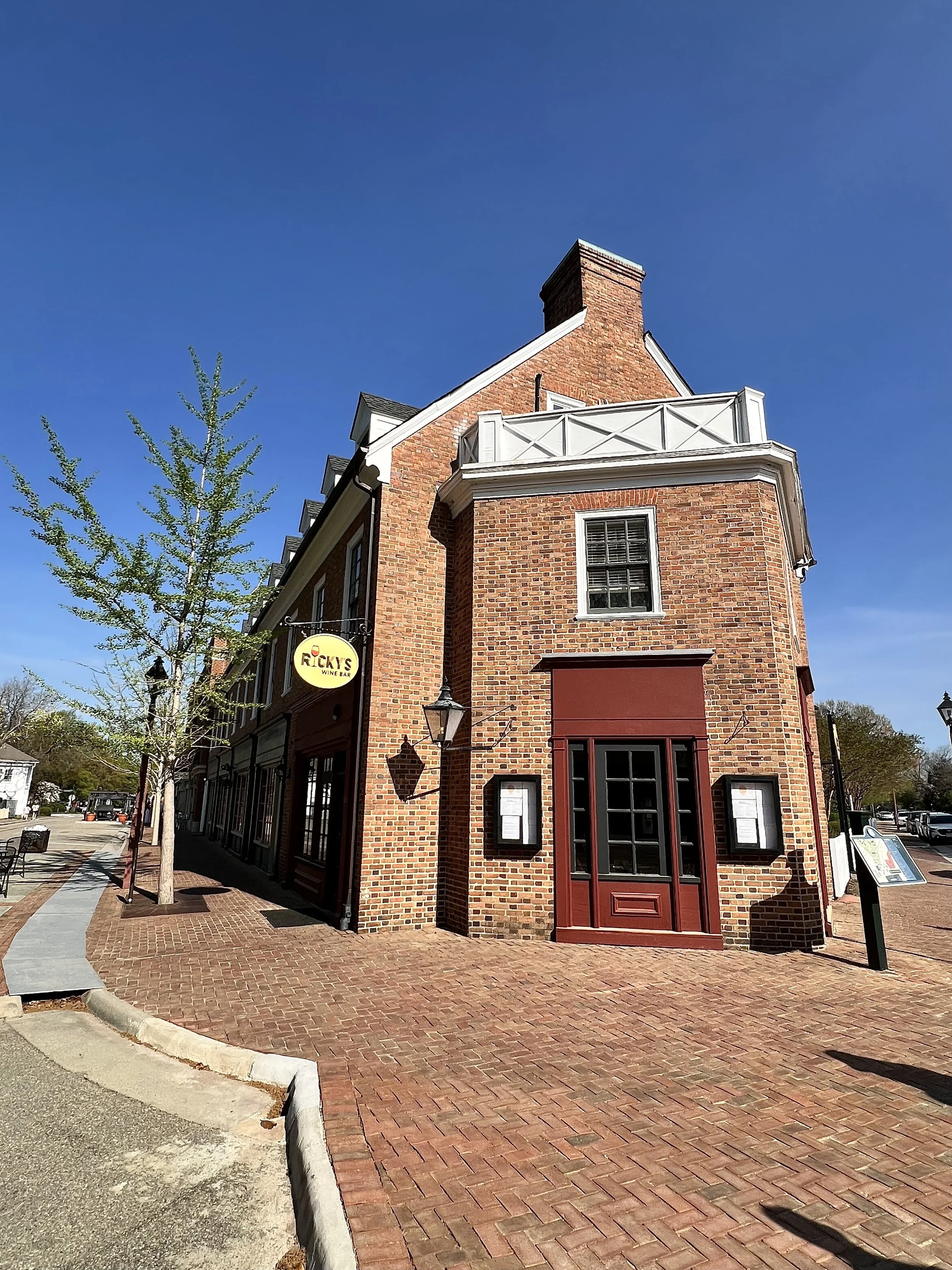 Brick building with a red door, black window frames, and a small white balcony, on a sunny day with a clear blue sky.