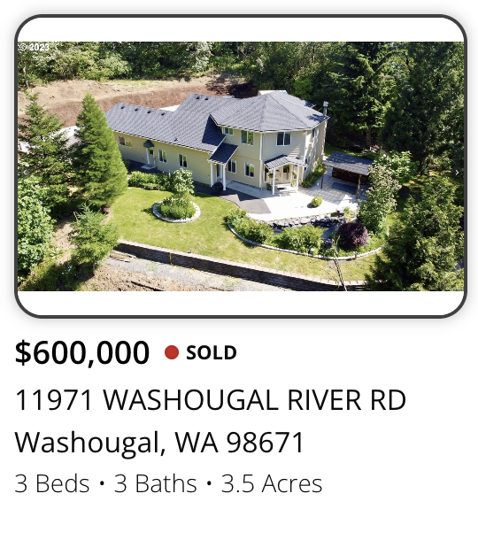 Aerial view of a two-story house with a landscaped front yard, surrounded by trees, with a driveway and outbuilding, located at 11971 Washougal River Road in Washougal, Washington.