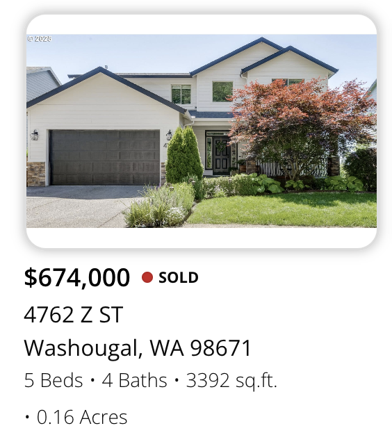 Front view of a two-story house with white exterior, black roof accents, a two-car garage, and landscaped yard with a red-leafed tree and green shrubbery.