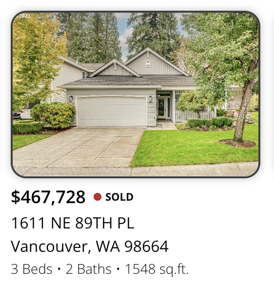 Front view of a gray house with a two-car garage, concrete driveway, and landscaped yard with trees and bushes.