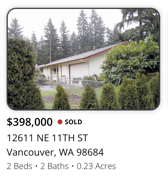 Single-story house with white exterior, red roof trim, surrounded by trees and bushes, located on a small lot.