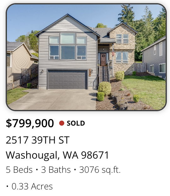 Front view of a two-story house with a gray garage door, a staircase leading to the main entrance, and a landscaped front yard with shrubs on a clear day.