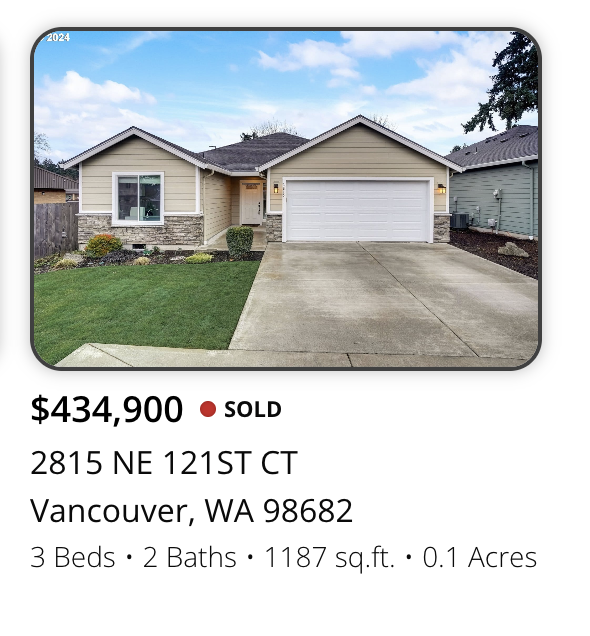 Front view of a single-story house with a two-car garage, manicured lawn, and suburban neighborhood. The house has beige siding, a stone accent on the lower part, and a small front porch.