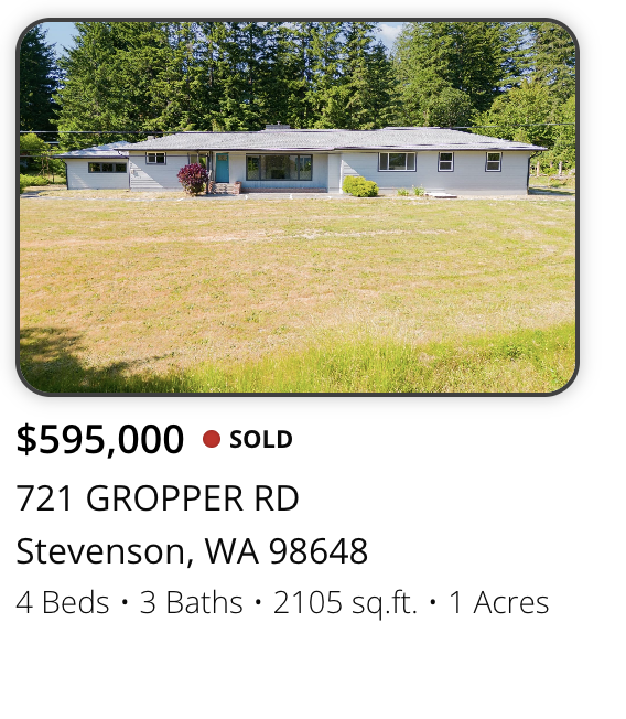 Single-story house with gray exterior, surrounded by green trees, on a large grassy lawn in Stevenson, Washington.
