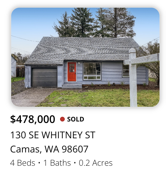 Front view of a house with grey siding, a red front door, attached garage, and a small front yard with grass and a white fence post