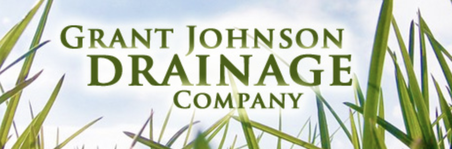 Sign for Grant Johnson Drainage Company against a background of green grass and a blue sky.