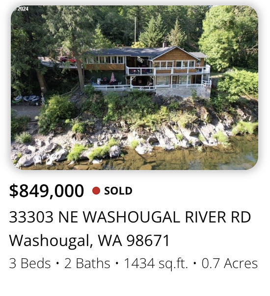 A house on a rocky shoreline surrounded by trees, with a deck and outdoor furniture, located at 33303 NE Washougal River Rd, Washougal, Washington.