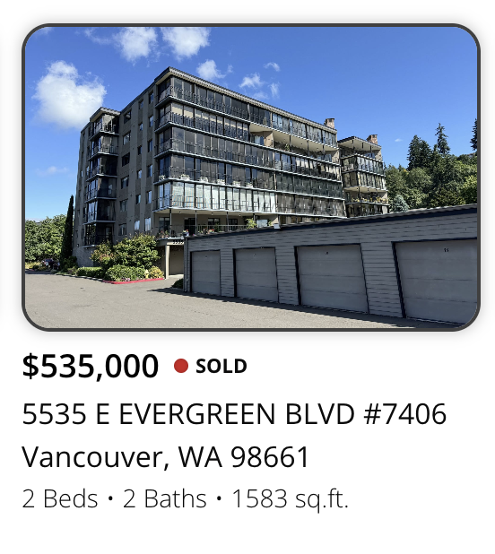 Exterior view of a modern, multi-story apartment building with glass balconies, located on E Evergreen Blvd in Vancouver, Washington, with a row of garage doors in the foreground.