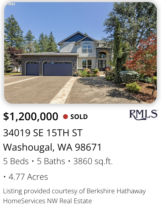 A Washougal Acreage estate sold by realtor Kelly Craig Graham. Front view of a large, two-story house with a three-car garage, blue and gray exterior, surrounded by trees and landscaping, on a sunny day.
