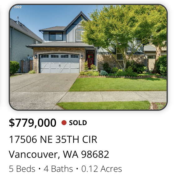 Front view of a two-story house with a gray and stone exterior, a green lawn, and a large tree in the yard. The house has a two-car garage and a porch with a red door.