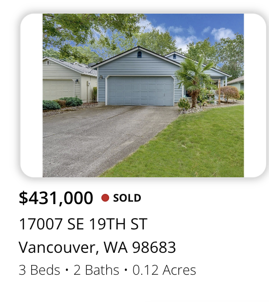 Front view of a blue house with a garage, driveway, green lawn, and surrounding trees, in Vancouver, Washington.