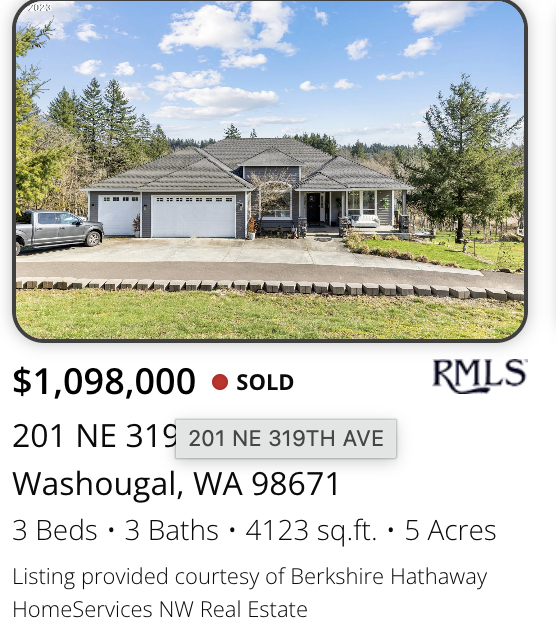 A rural  5 acre Washougal property sold by Kelly Craig Grahan with a attached two-car garage, surrounded by greenery, under a partly cloudy sky. The house has a front porch and a driveway, with a car parked on the left side.