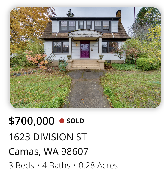 Front view of a white, two-story house with a purple front door, small porch, and concrete steps, surrounded by trees and grass, on a slightly overcast day.