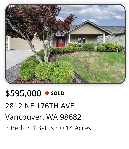 Front view of a single-story house with a manicured front yard featuring trimmed bushes, a tree with reddish leaves, and a green lawn. The house has beige siding, a gray roof, and a porch with a red door.