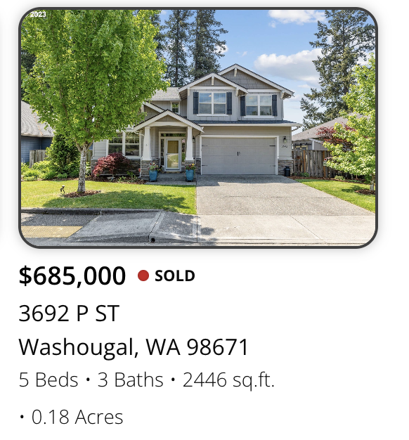 Photo of a two-story house with a grey roof, white siding, and a two-car garage, surrounded by greenery in Washougal, Washington.