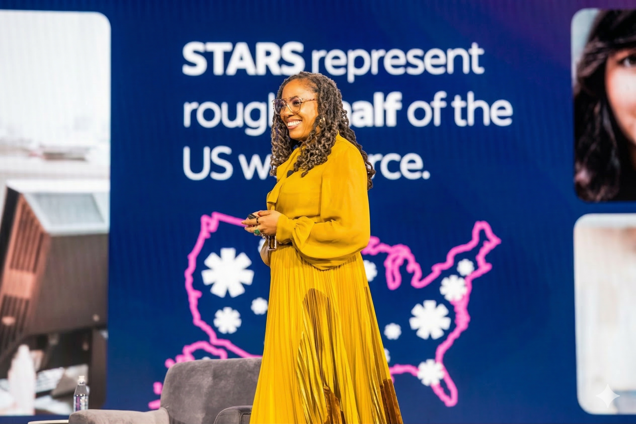 A woman in a yellow dress smiling on stage at a conference, with a large screen behind her displaying a map of the United States and text about the US workforce.