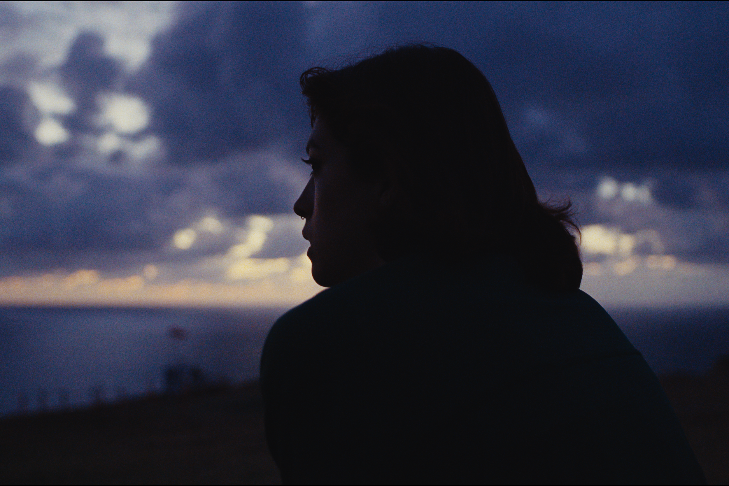 Silhouette of a person with long hair looking to the left against a cloudy evening sky.