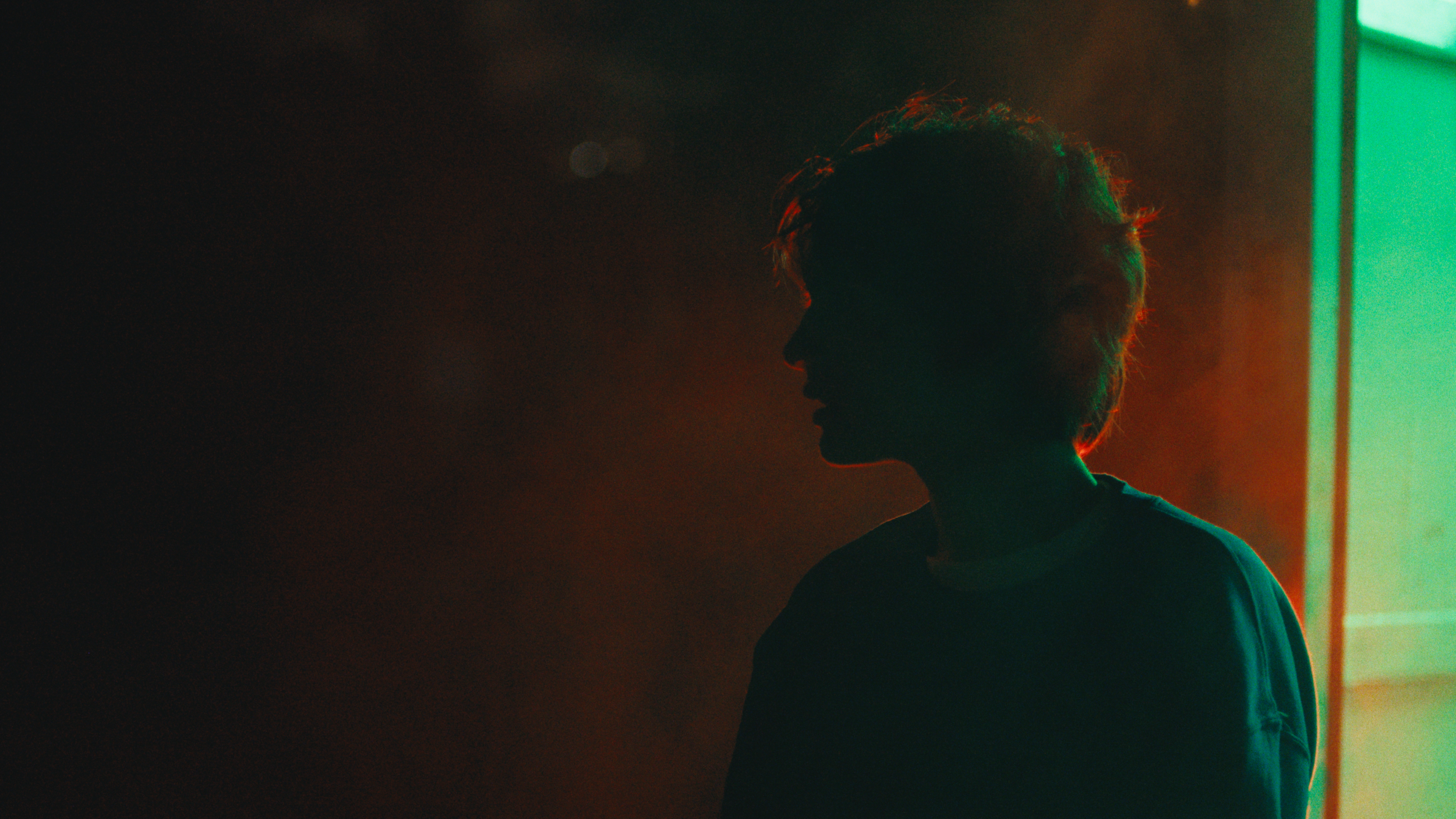 Silhouette of a person with curly hair in front of colorful neon lighting, with a dark background.
