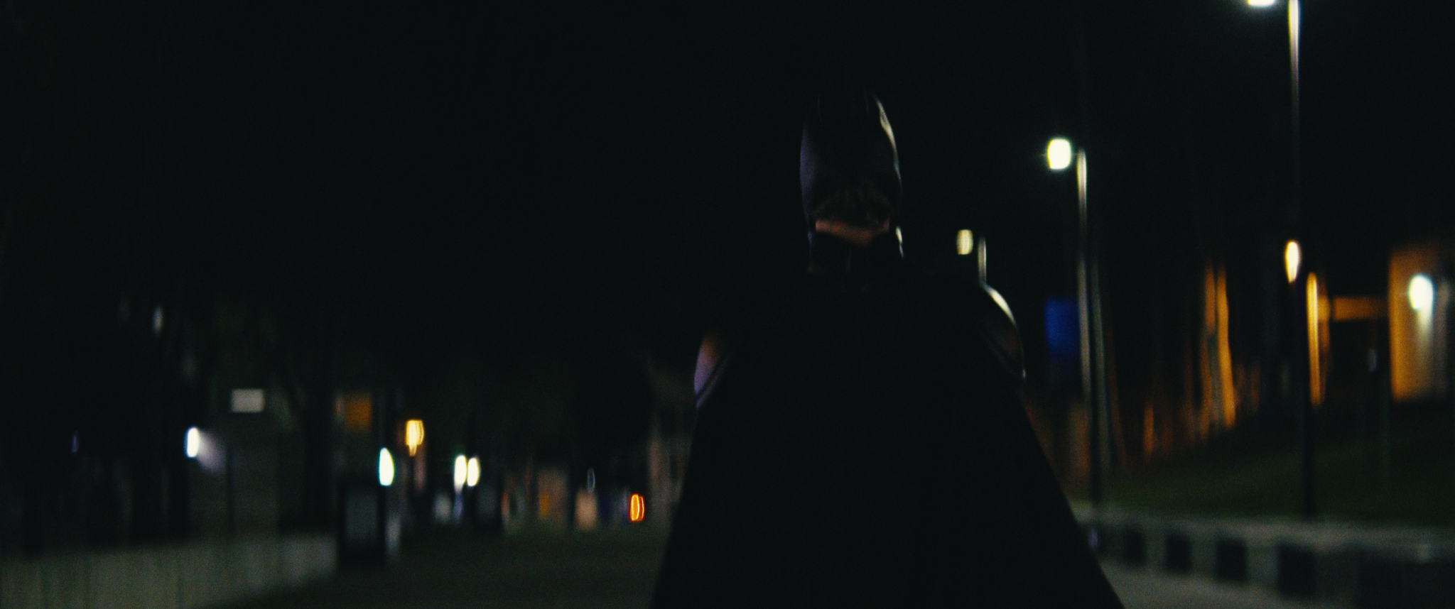 A person wearing a hooded jacket walking at night in an urban area, illuminated by streetlights.