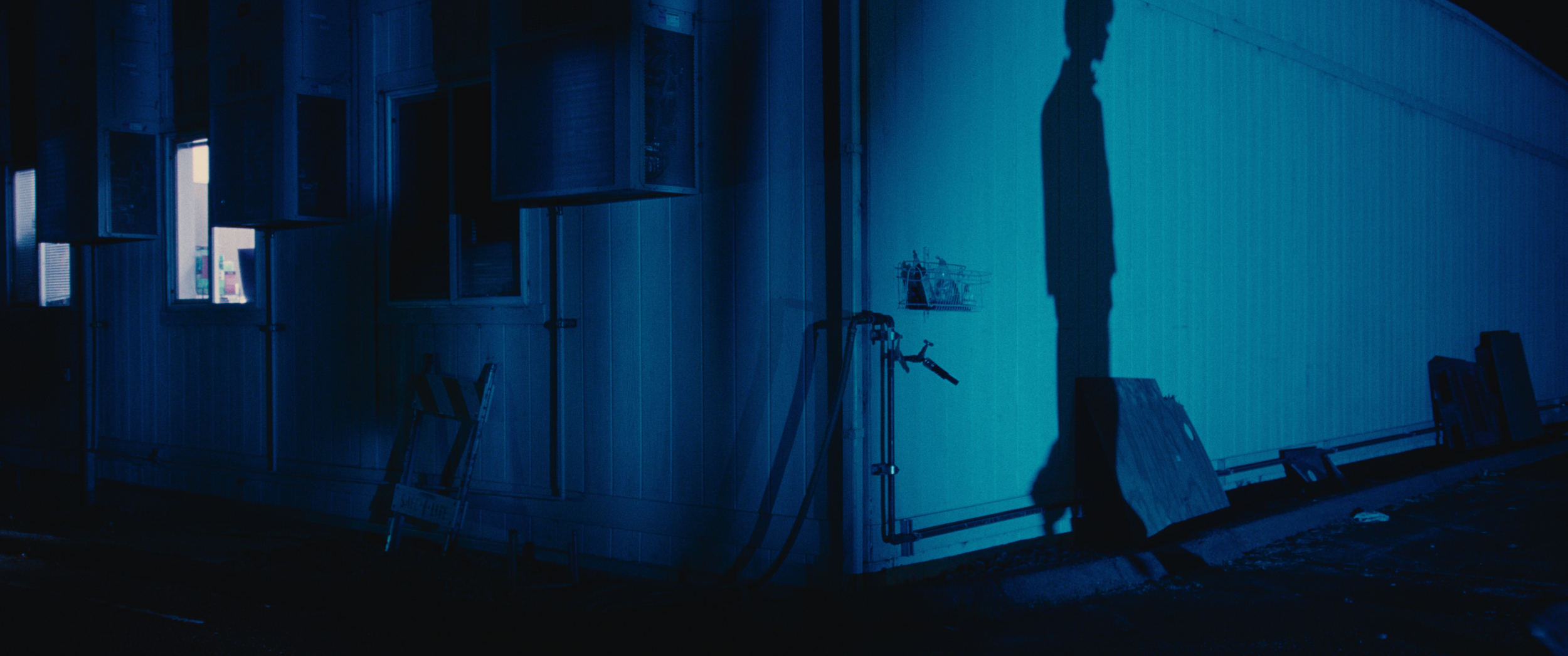 Shadow of a person cast on the side of a building with construction materials and tools nearby at night.