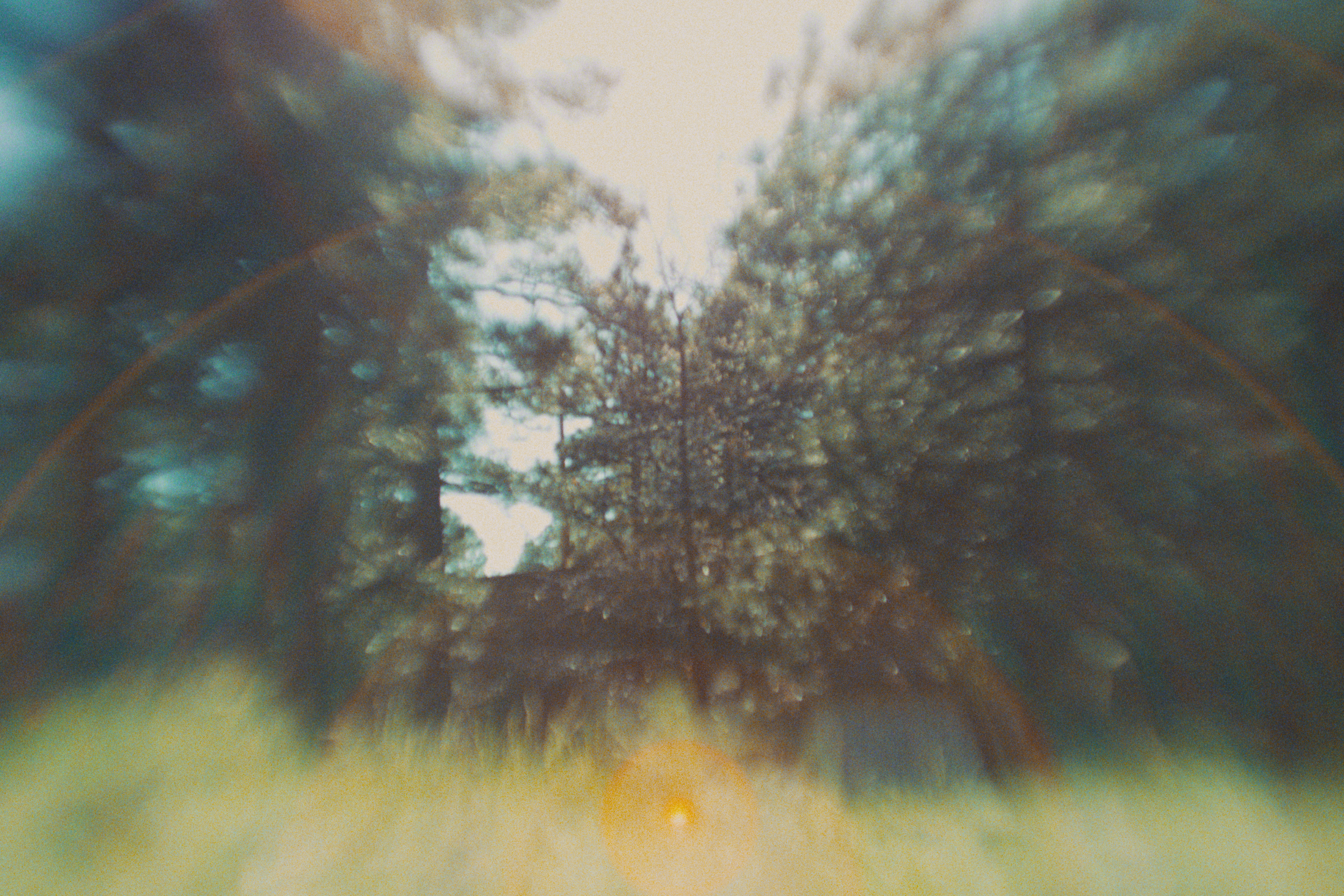 A view looking up into a sky filled with dark, dramatic clouds. A bright light is seen through the clouds, creating a rainbow-like reflection and lens flare effects.