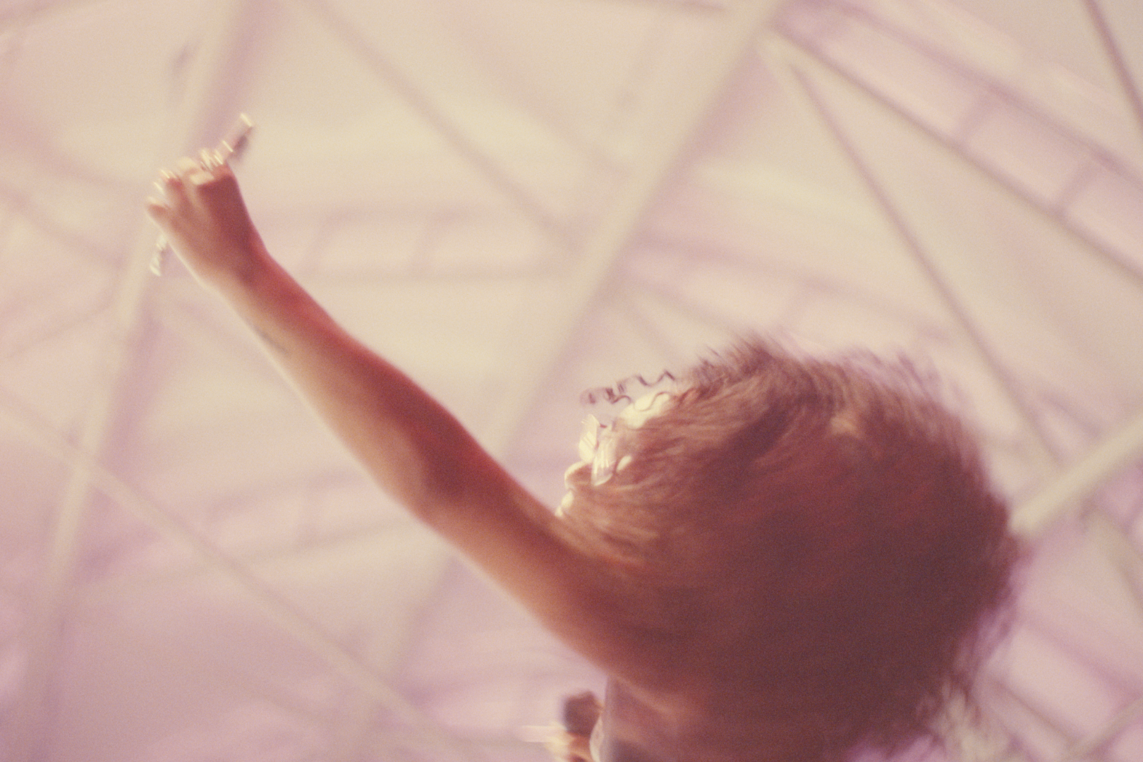 A person with curly hair reaching up on an escalator, viewed from below with a blurry background.