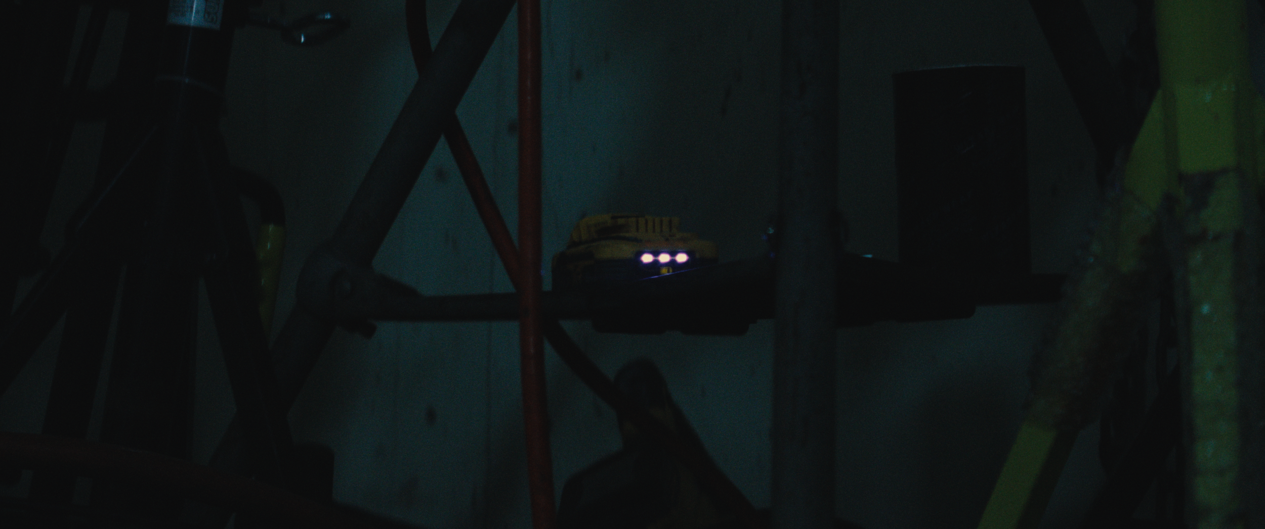 Dimly lit workshop with a yellow toy car on a shelf, surrounded by metal and wooden parts.