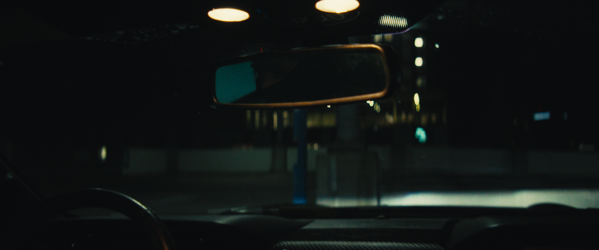 Nighttime view from inside a car showing the rearview mirror and dark street outside with faint streetlights.