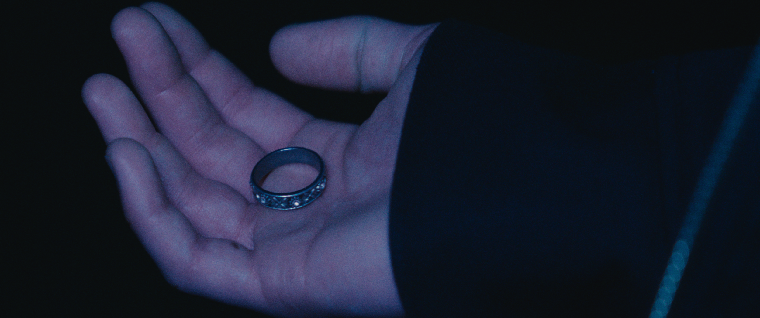 A person's hand holding a silver ring with intricate designs against a dark background.