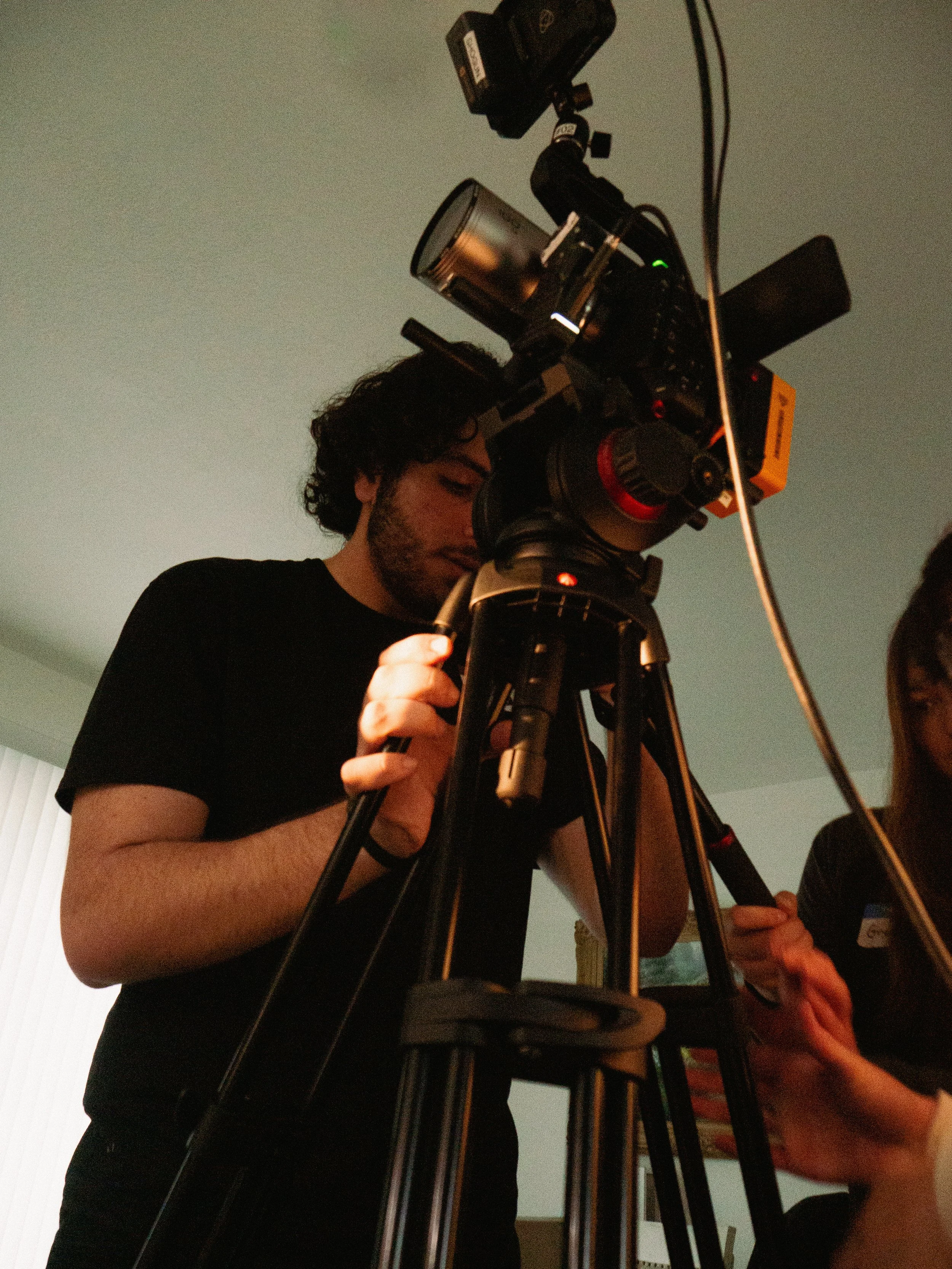 A person looking through a professional camera on a tripod, setting up or taking a photo indoors.