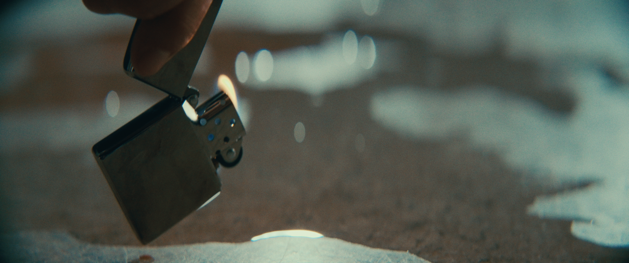 Close-up of a hand holding a metal lighter, lighting a fire on a surface.