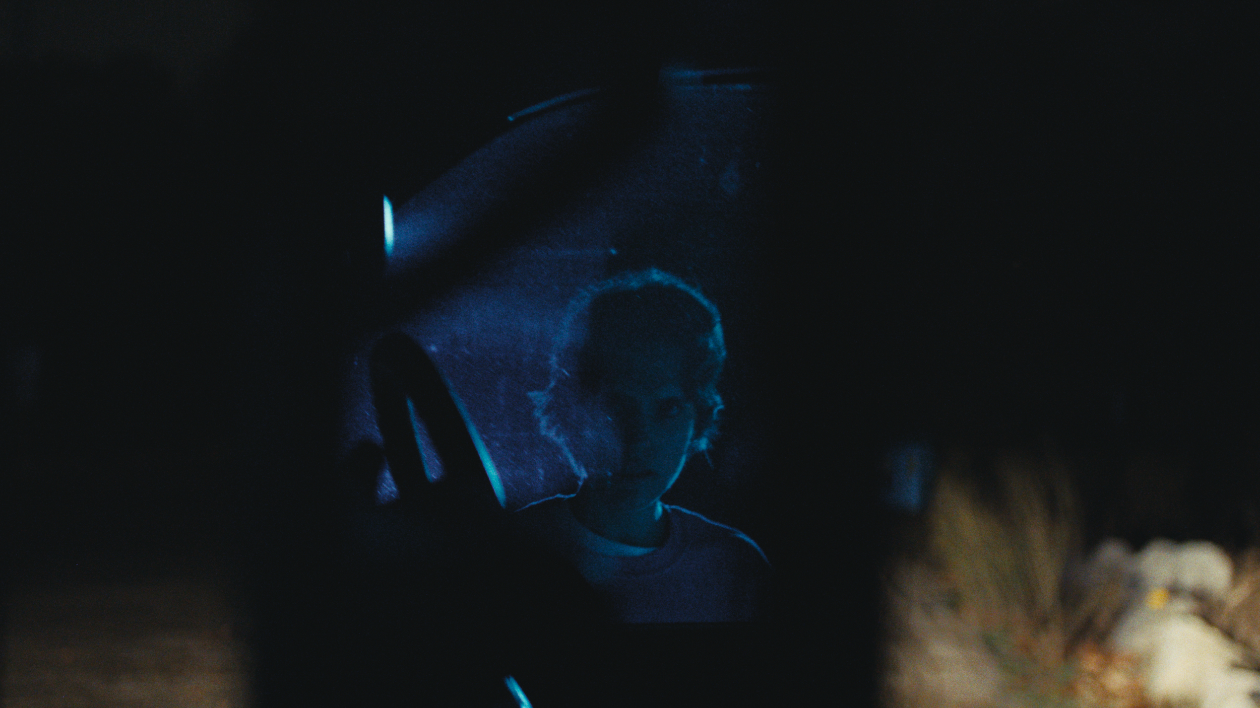 A person wearing glasses and a cap stands in a dark environment illuminated by blue light, with their face partially visible.