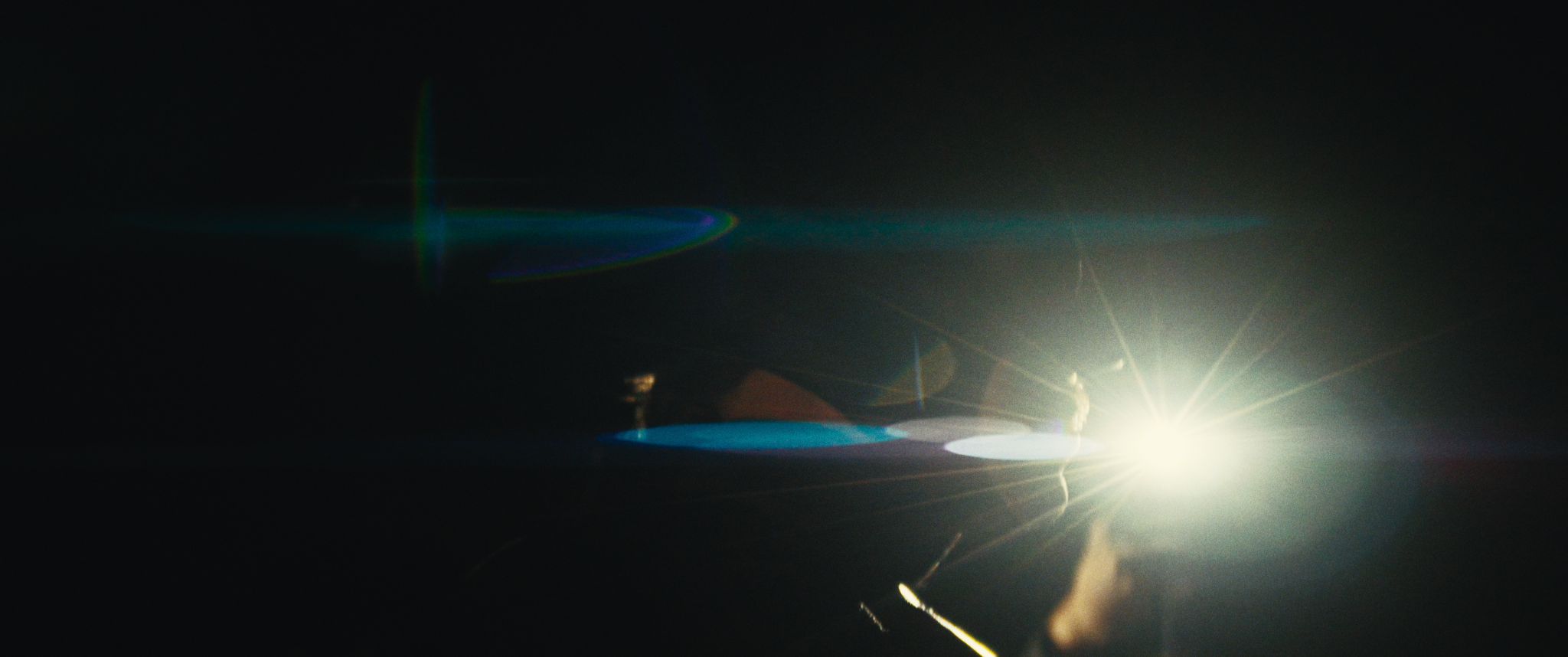 Bright light source emitting lens flares and rainbow-colored reflections in darkness.