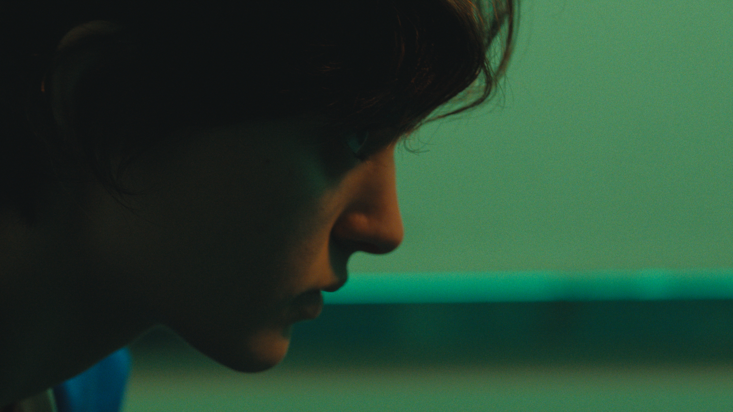 Close-up of a person's face in profile with dark, wavy hair against a green background.