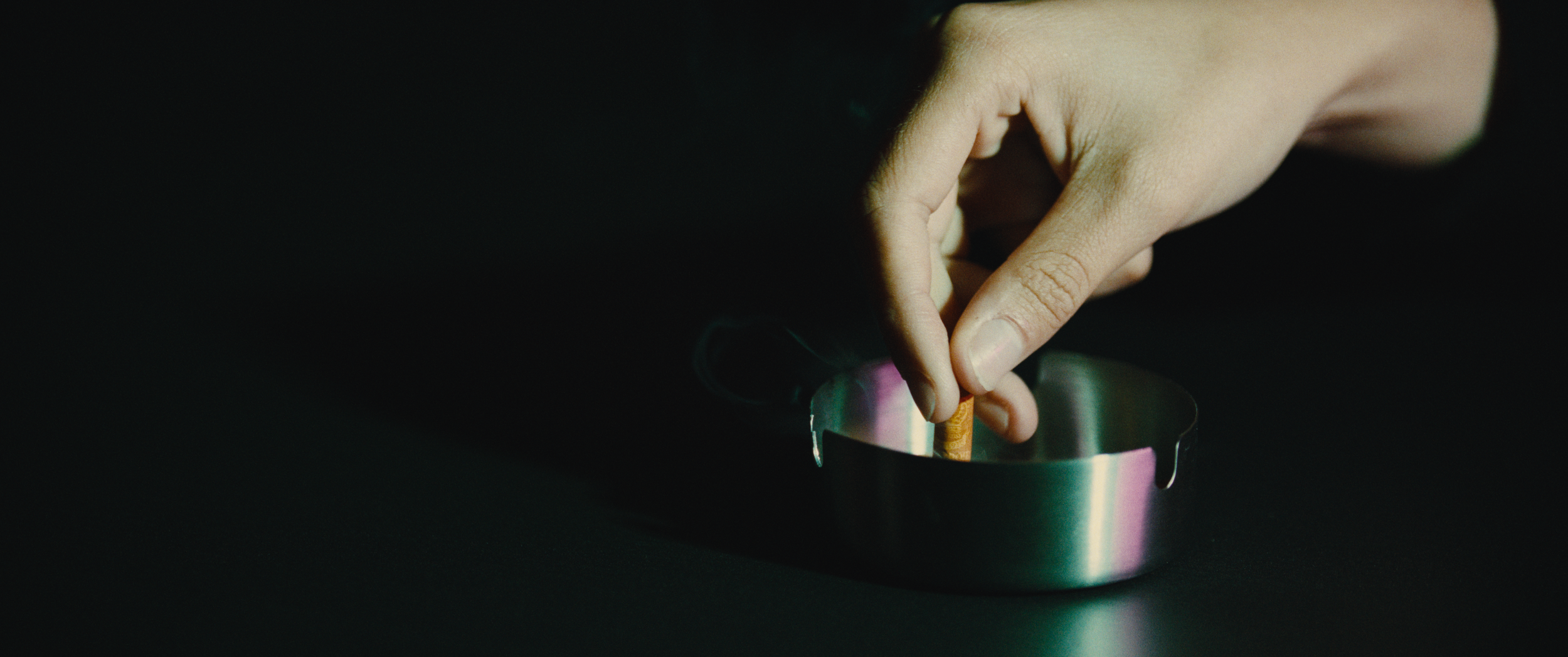 Close-up of a hand lighting a cigarette with a match in a dark setting.