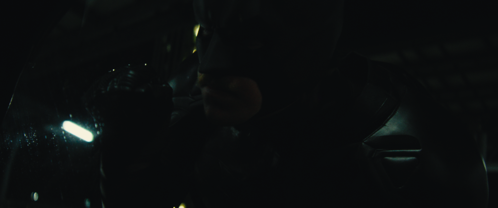 A dark image showing a person in a suit and gloves holding a glowing object in their hand.
