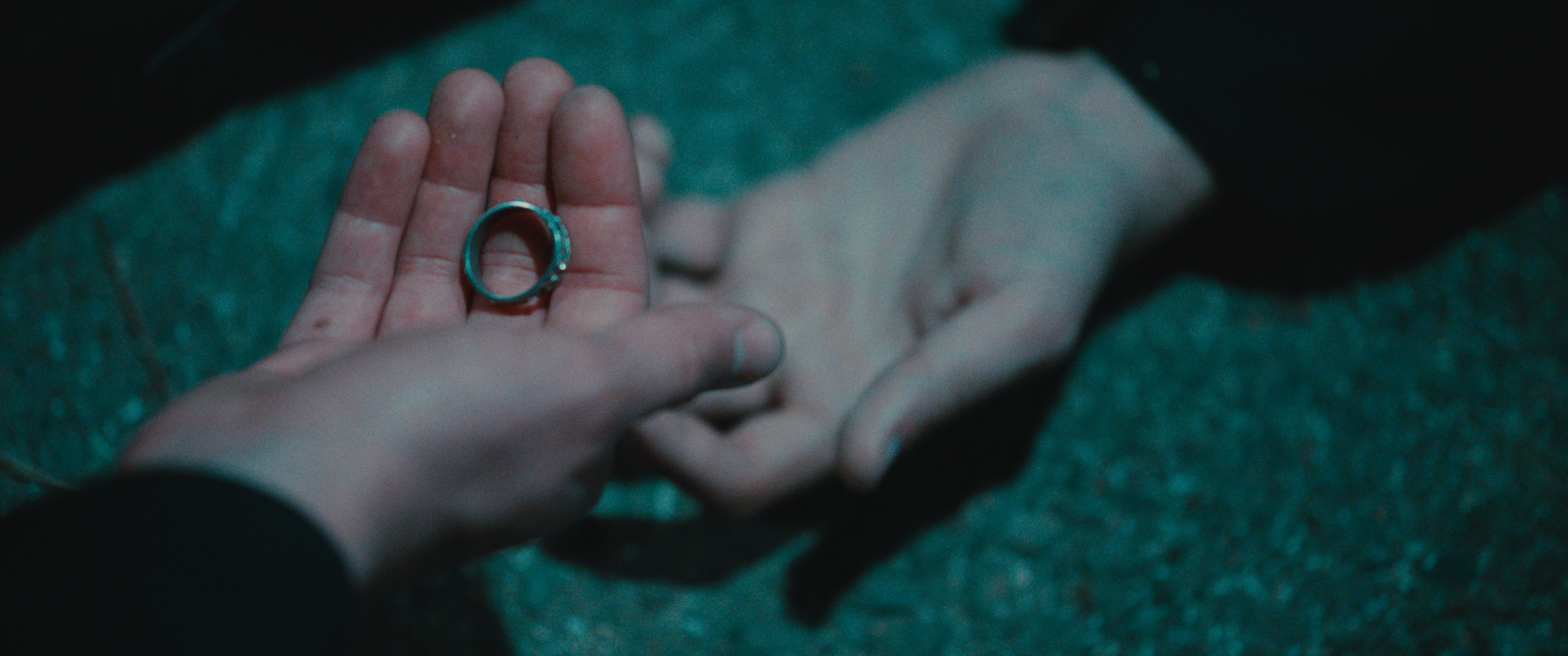 Person holding a silver engagement ring over the hand of another person lying on a green carpet.