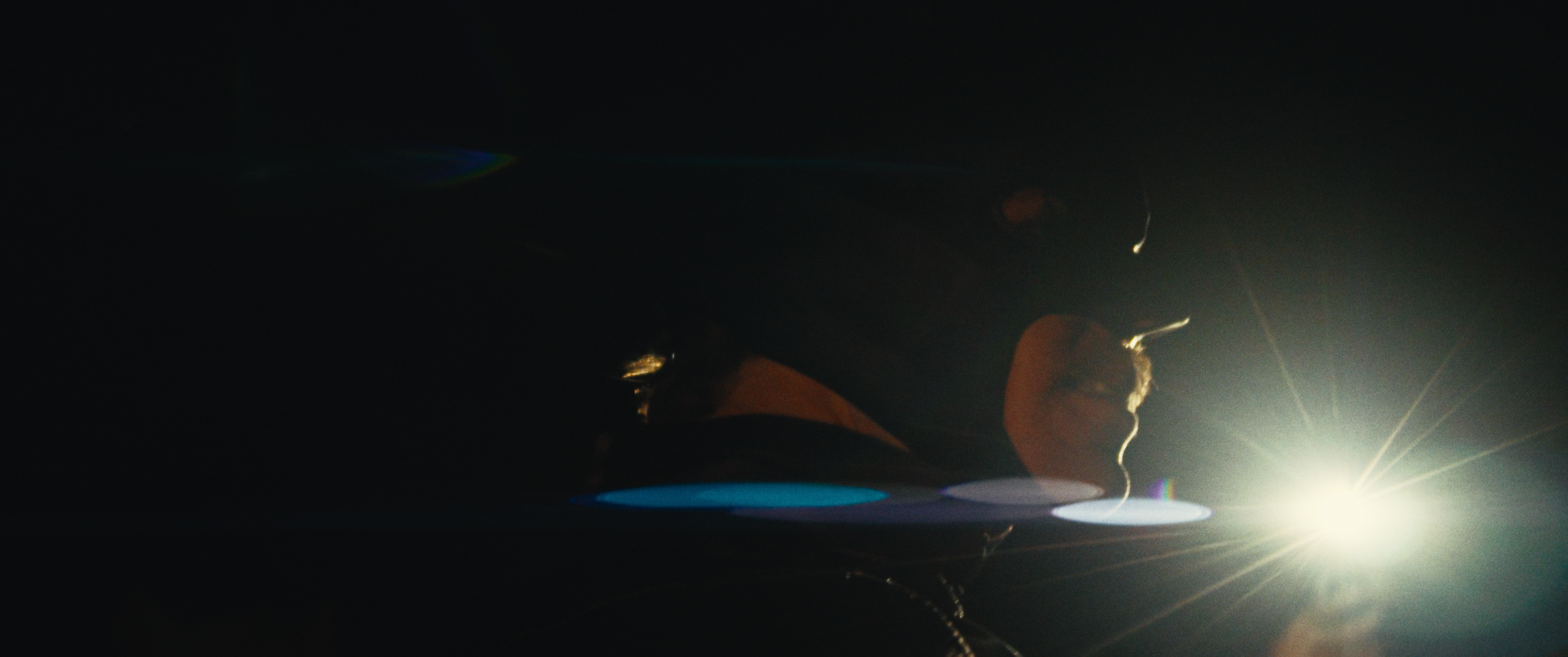 Person pointing towards a bright light source in dark surroundings with lens flare effects.