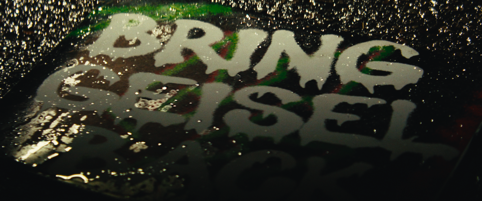 Close-up of a metallic surface with the word BAPE engraved, with water droplets and reflective colors.