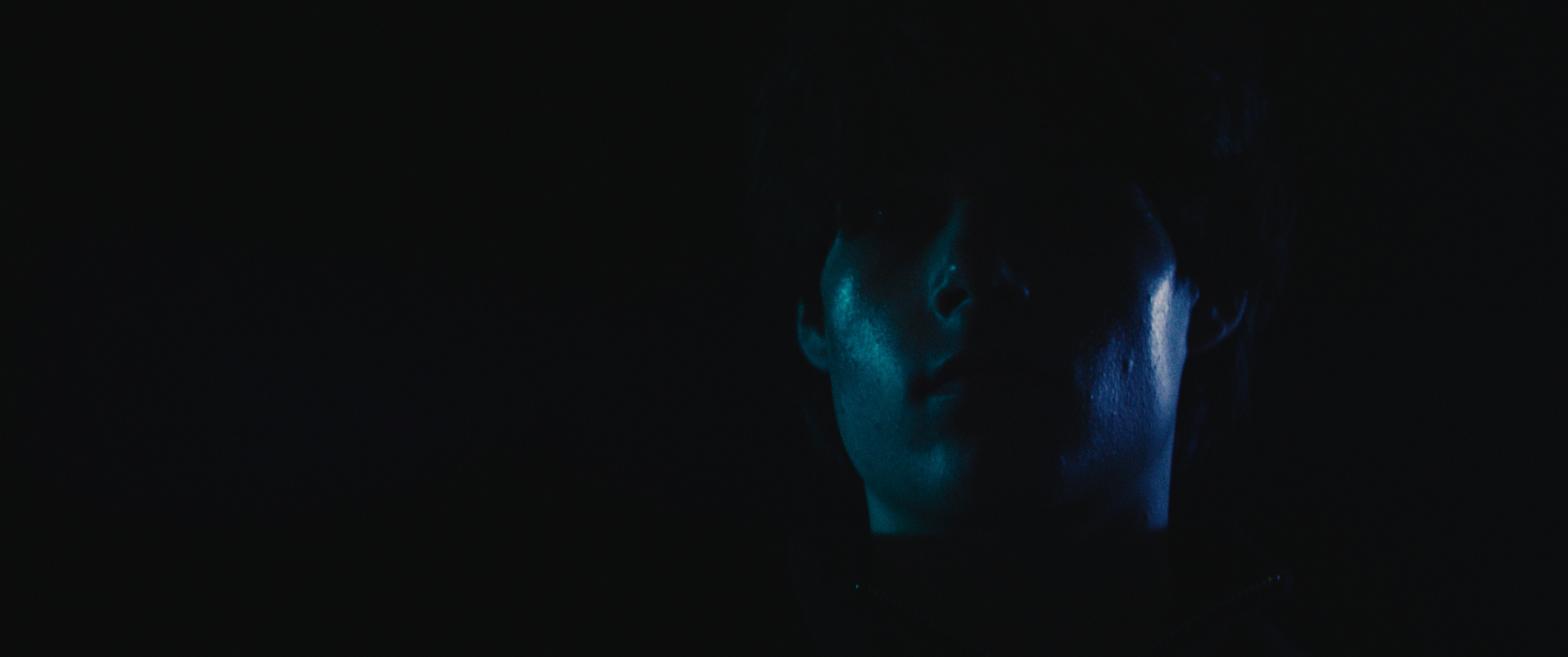 A person's face partially illuminated by blue light in a dark setting.
