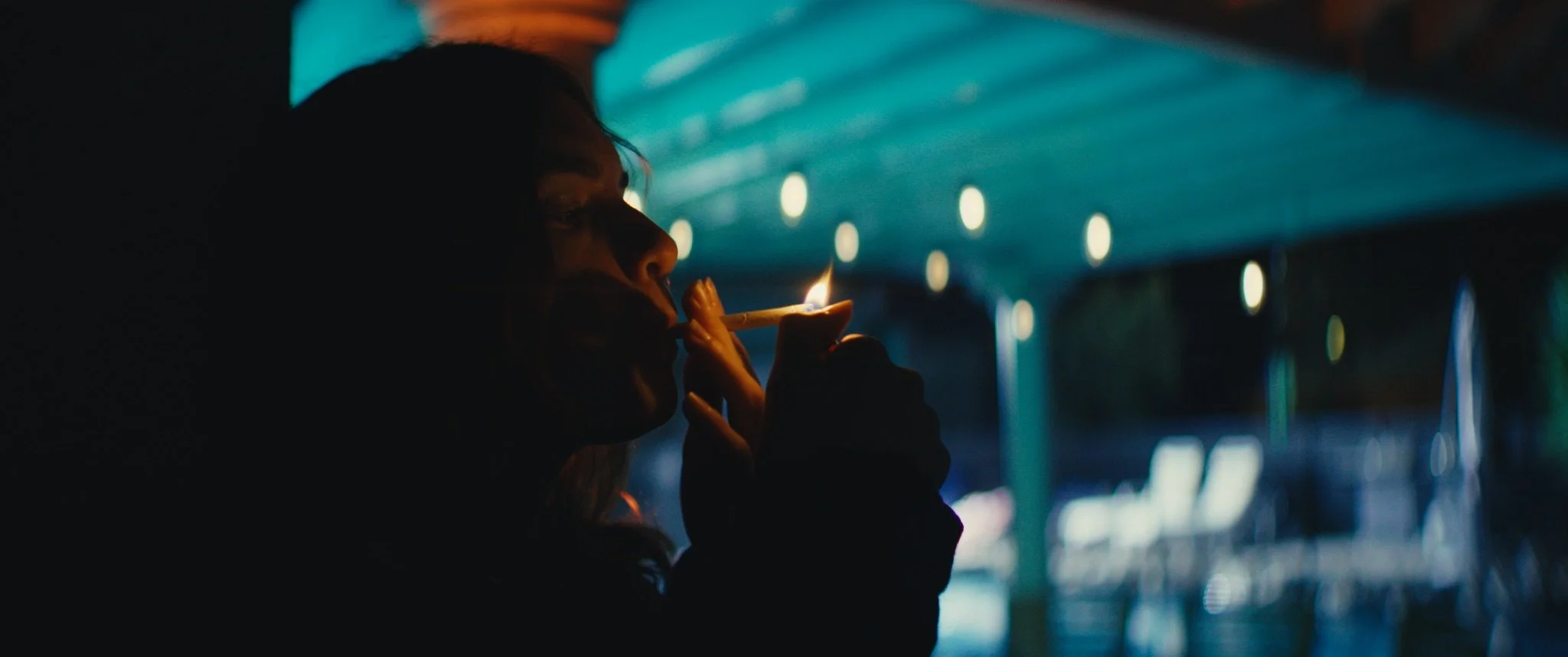 Person lighting a cigarette in a dimly lit area with blue lights and blurred background.
