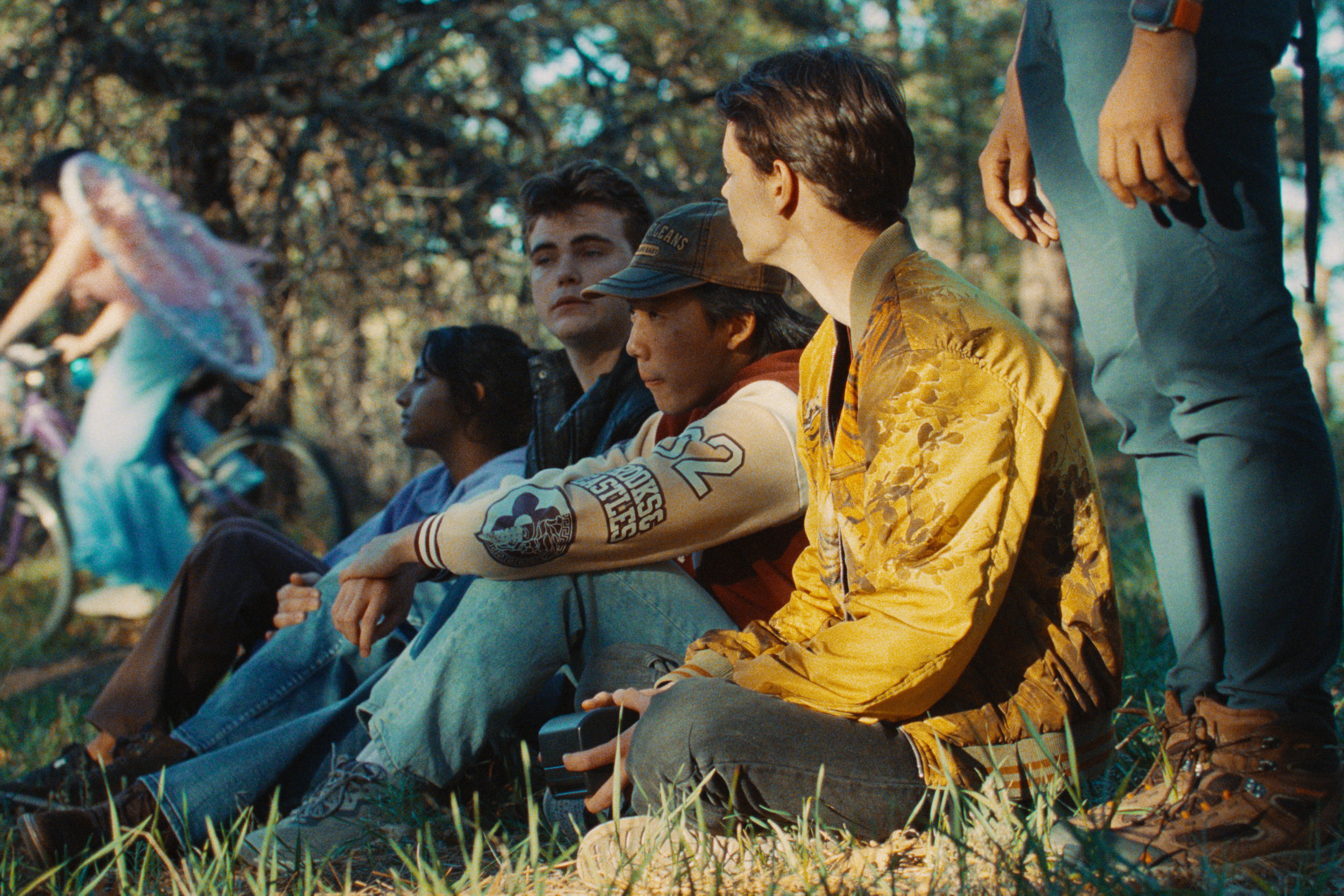 A group of young people sitting outdoors on grass in a park, engaging in conversation and relaxing on a sunny day.